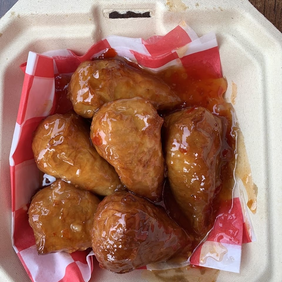 THE KRAZY VEGAN's sweet and sour vegan wings in a takeout container with red and white checkered paper.