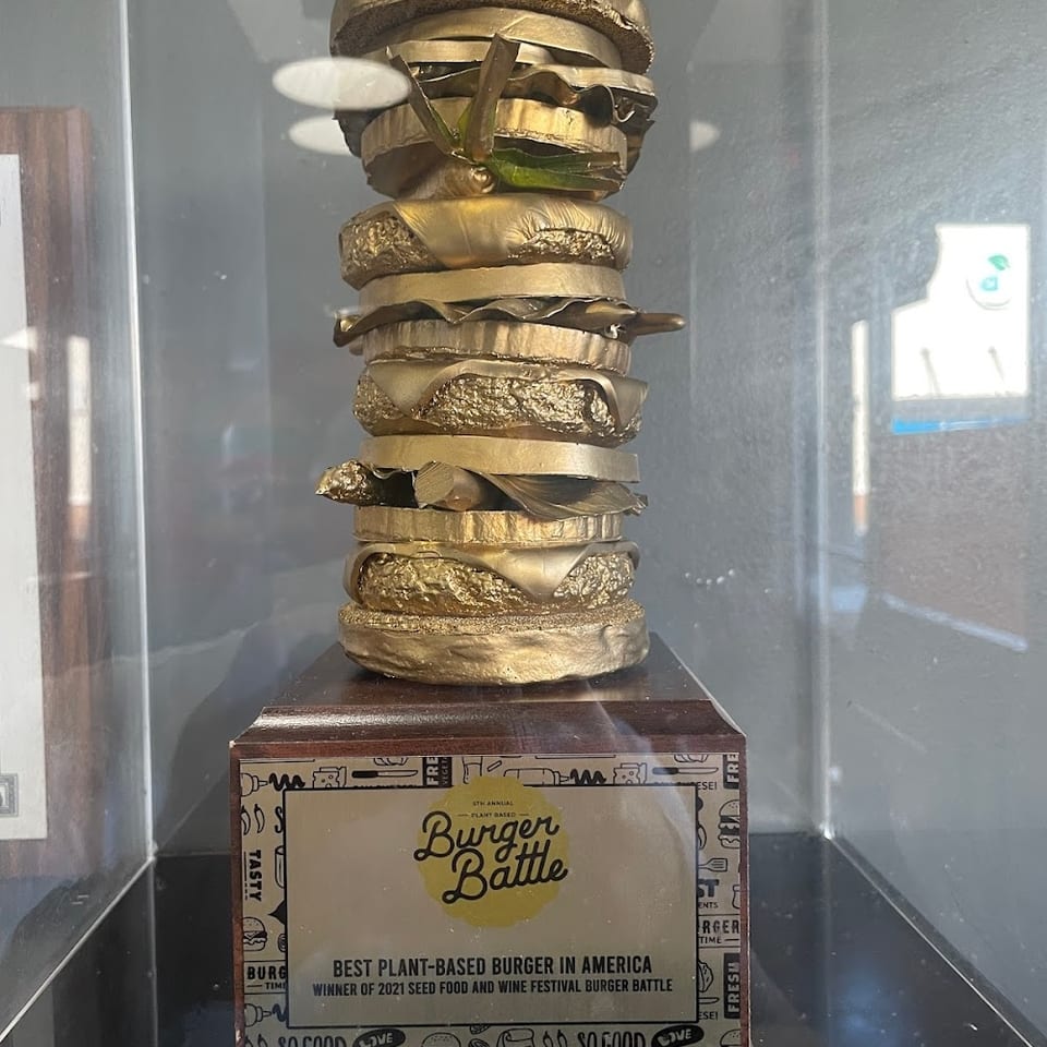 A golden burger trophy, awarded for "Best Plant-Based Burger in America" to THE KRAZY VEGAN.