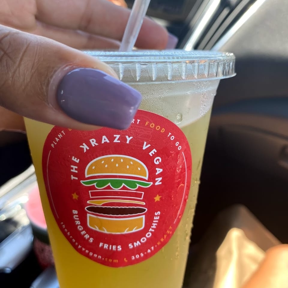 Hand with purple nails holding a clear cup with a Krazy Vegan logo and a straw.