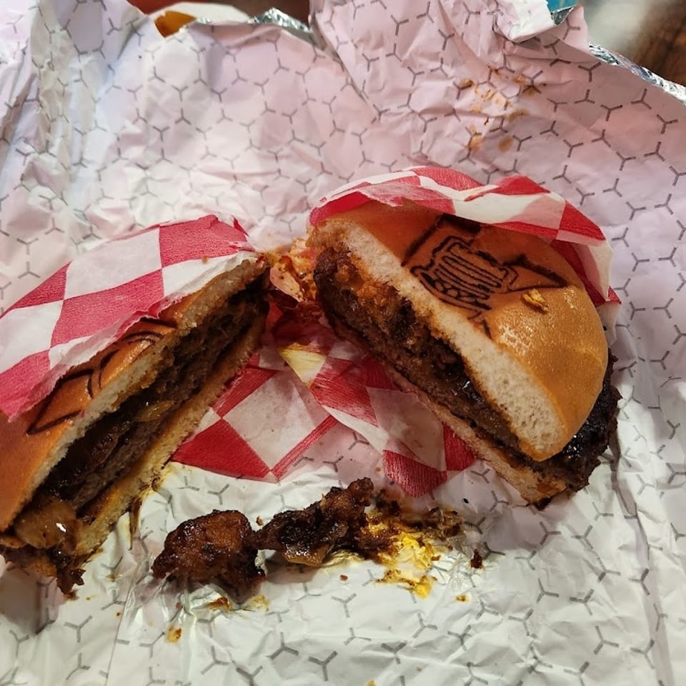 A Krazy Vegan burger, cut in half, revealing a thick patty and toppings, on crumpled wrapper.