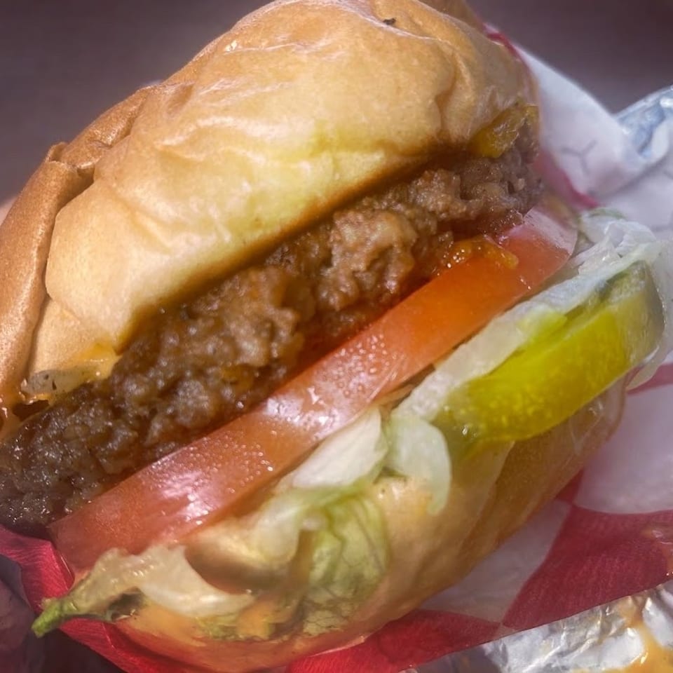 A Krazy Vegan burger with a patty, tomato, lettuce, and pickles in a bun.